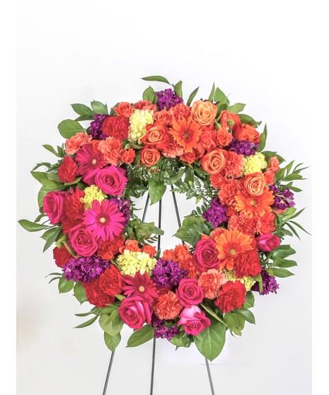 Wreath display featuring a mix of lush pink and lavender flowers including roses, carnations, and daisy's displayed on an easel. 