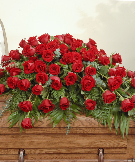 Red roses with lush greens are artfully designed to make a statement in this casket spray. 